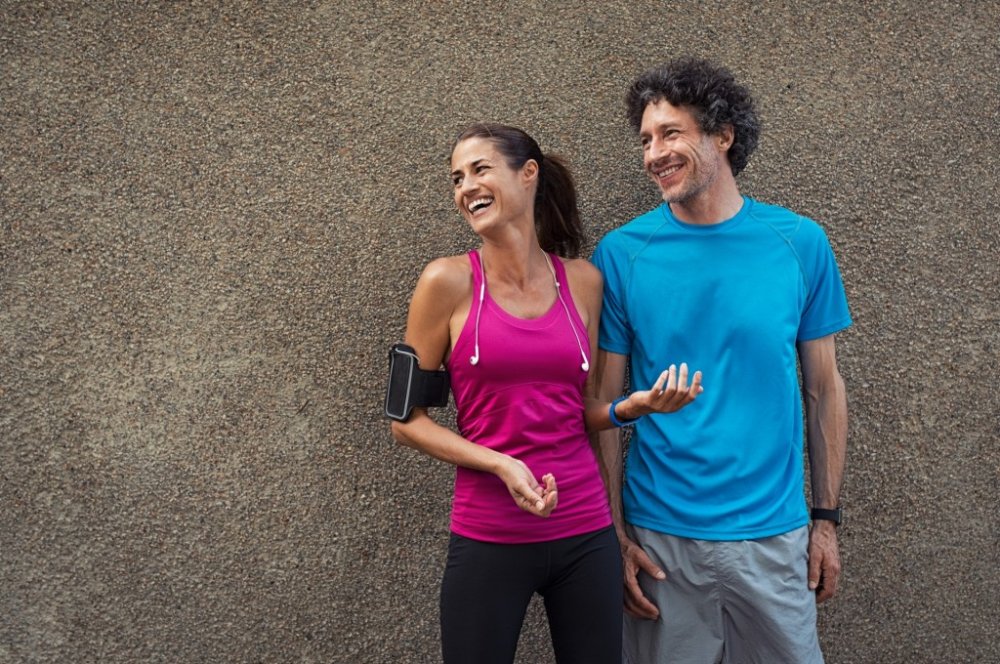 Muž a žena ve sportovním oblečení stojí u zdi a smějí se