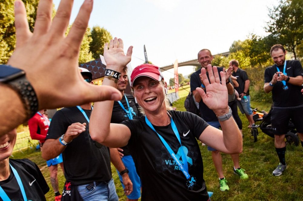 Žena v kšiltovce a tričku Vltava Run běží, zeširoka se usmívá a natahuje a připravuje ruce k plácnutí (high five).