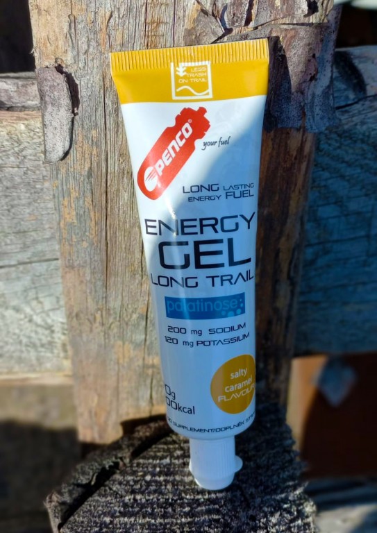 Bílo-žlutá tuba Penco Energy Gel Long Trail postavená na dřevěném sloupku. Na obalu je viditelný nápis palatinose a informace o obsahu sodíku a draslíku.