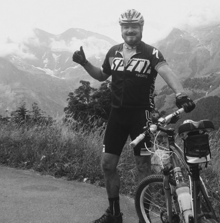 Vladimír Hrabec v cyklo dresu a s kolem uprostřed hor - černobílá fotografie