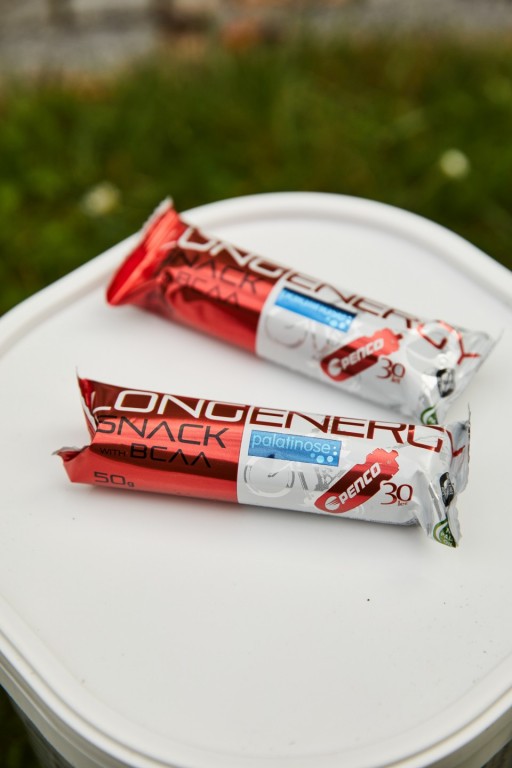 Dvě Penco tyčinky Long Energy Snack leží na bílém plastovém boxu.