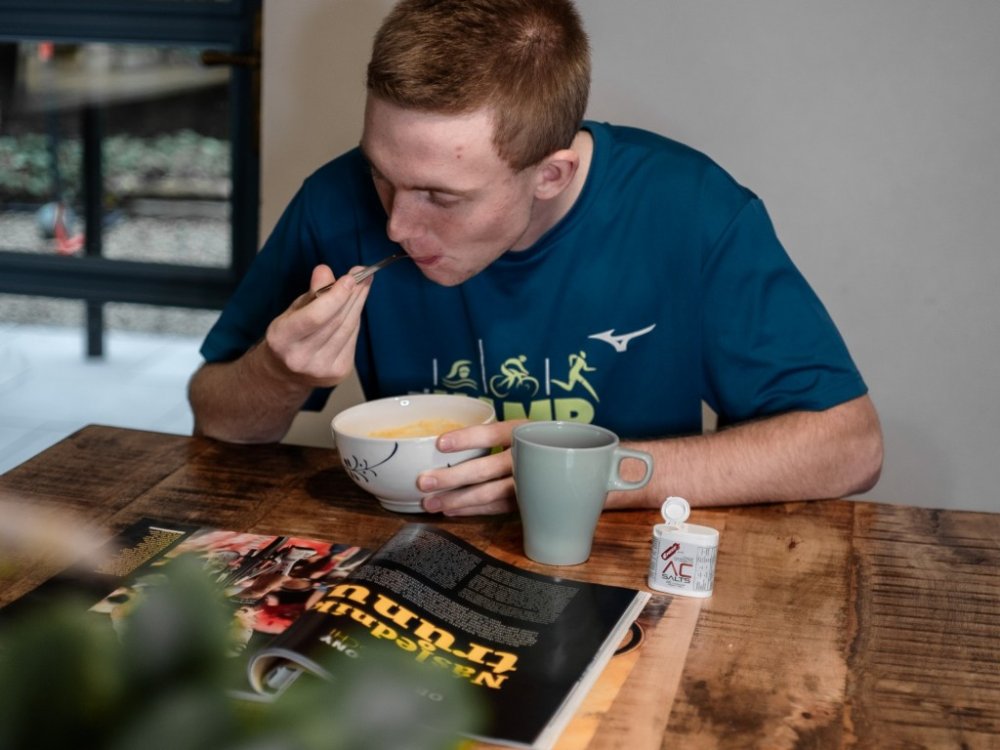 Mladý muž sedí u kuchyňského stolu a jí kaši Pelupa od Penco.