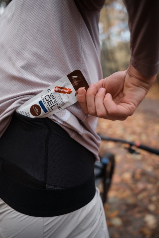 Detailní záběr na záda sportovce, který si z kapsy v bederním pásu vytahuje energetický gel Penco.
