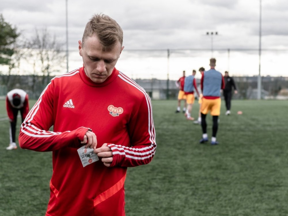Fotbalista v červeném dresu je na fotbalovém hřišti a rozbaluje si X_Ride Shot od Penca