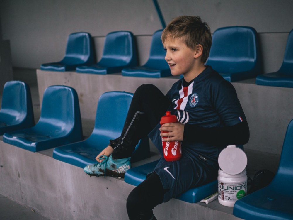 Chlapec sedí na tribuně a v rukou drží červený bidon Penco